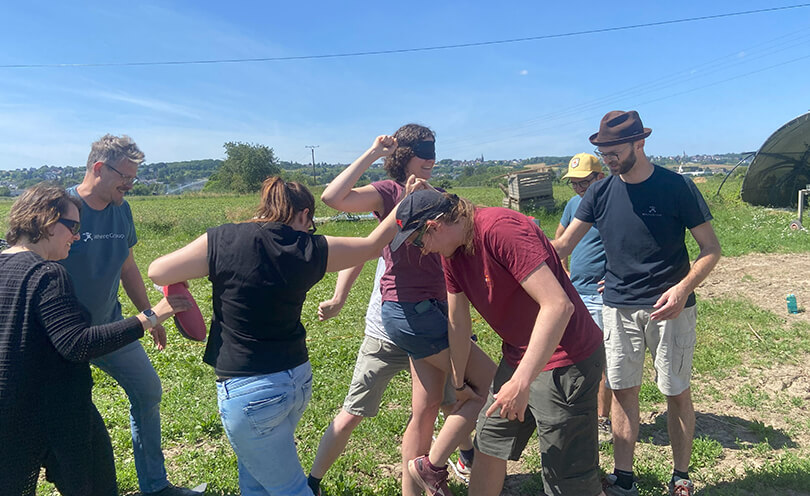 Sieben Personen auf einem Feld, eine Person hat die Augen verbunden. Teambuilding.