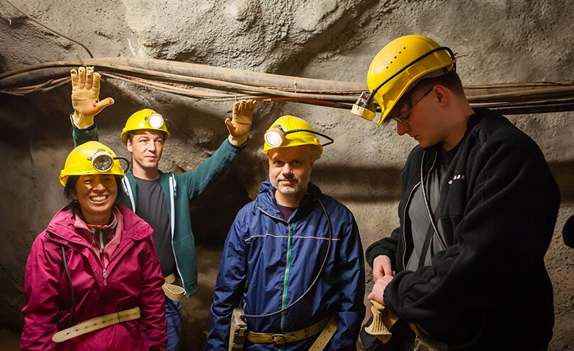 Vier Personen in einem Bergwerk, eine Person hat die Arme nach oben gestreckt. Open Source GIS.